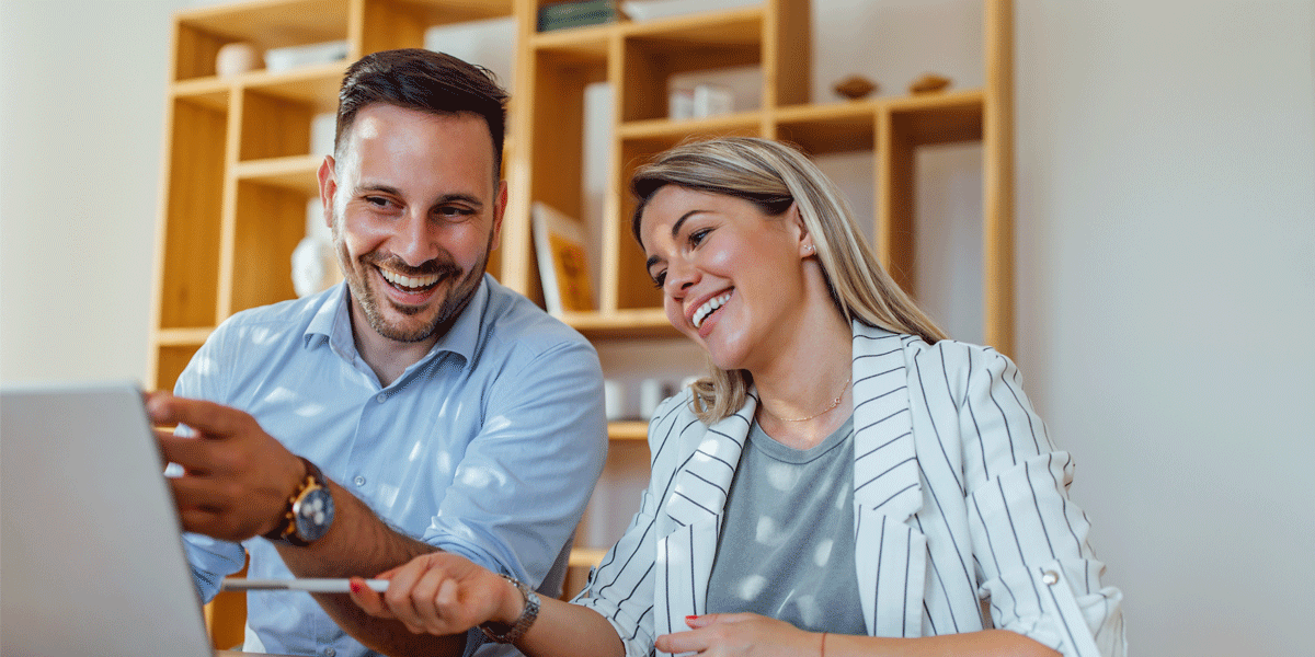 A man and woman laughing together while looking at a laptop.